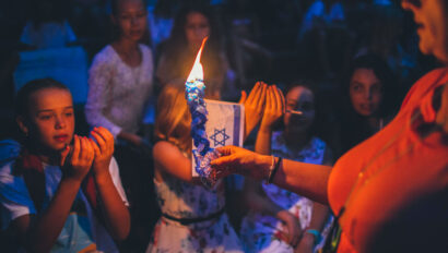 woman holding a candle in the dark with an israeli flag in the background.