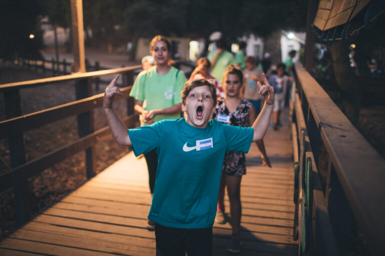 excited kid with his hands in the air at night walking in front of a group of kids and teens.
