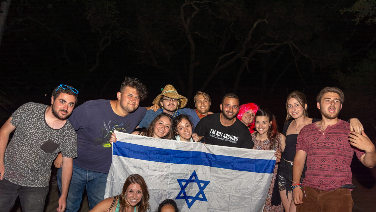 group of teens holding up an israeli flag at night.