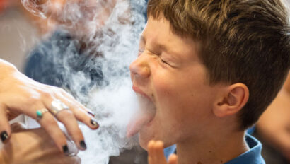 kid with mouth open and breathing in gas from a speaker as part of a science experiment.