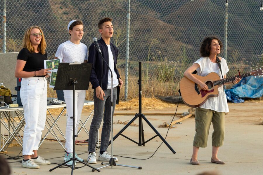 three teens singing outside while a woman plays a guitar.