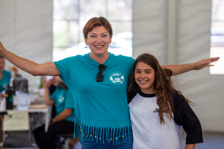 camp staff member with her hands stretched wide and a camper next to her.