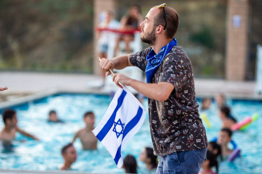 man waving an israeli flag next to a swimming pool.
